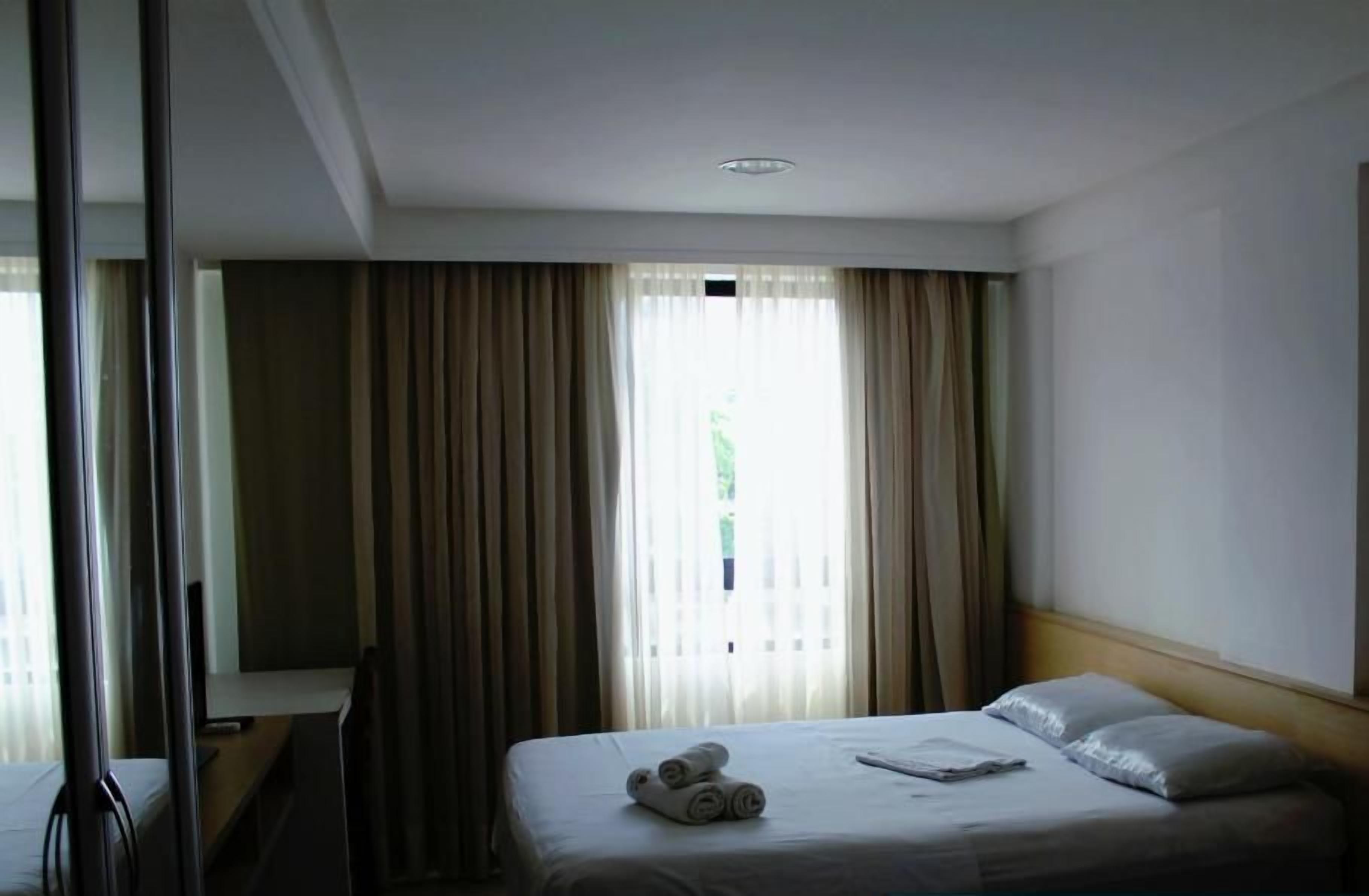 Habitación de hotel con dos camas, un escritorio y un amplio ventanal con cortinas.