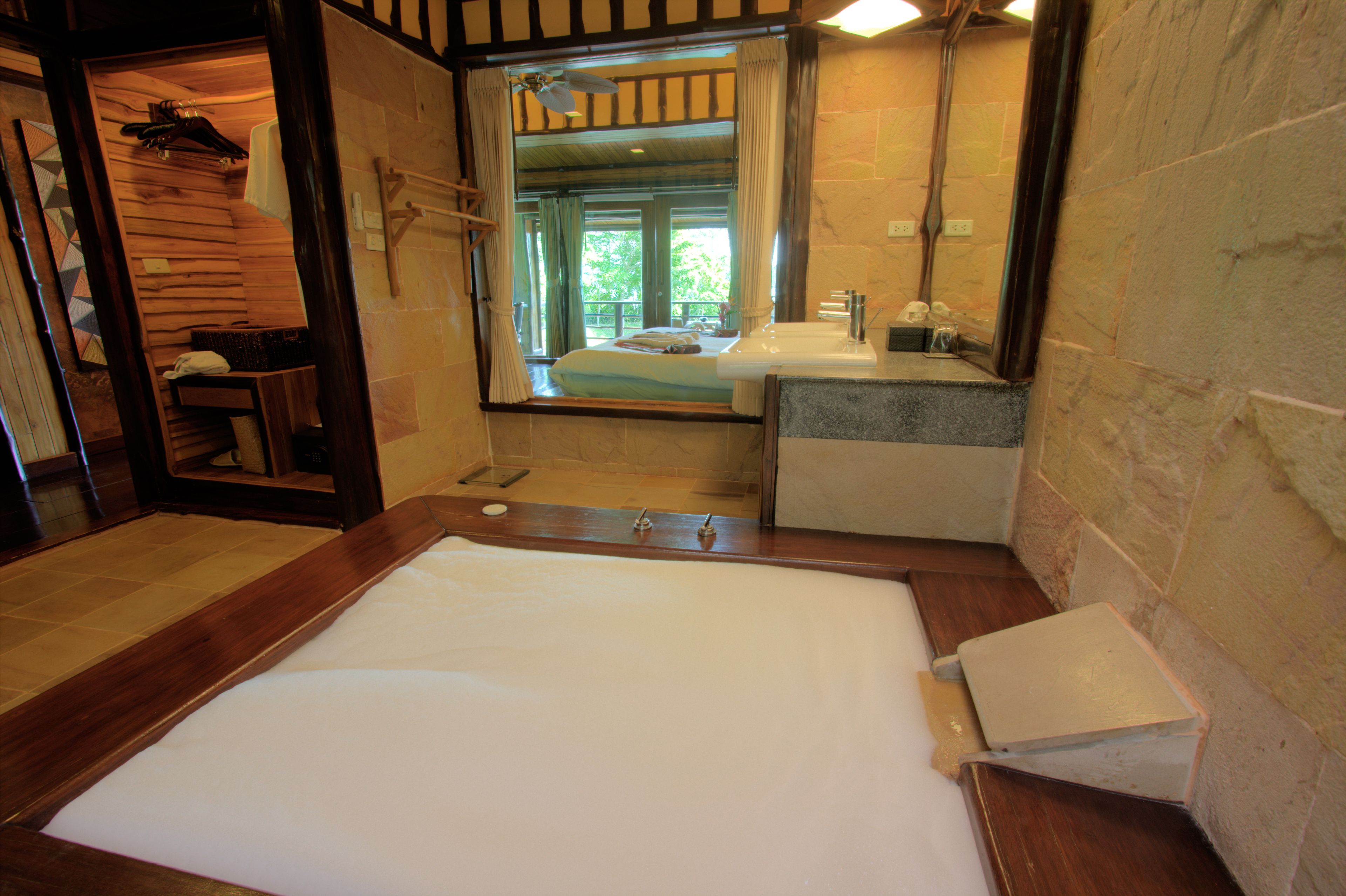 Une chambre à coucher de style cabane en bois, avec un grand lit, un banc en bois et une vue sur l’extérieur par une fenêtre.