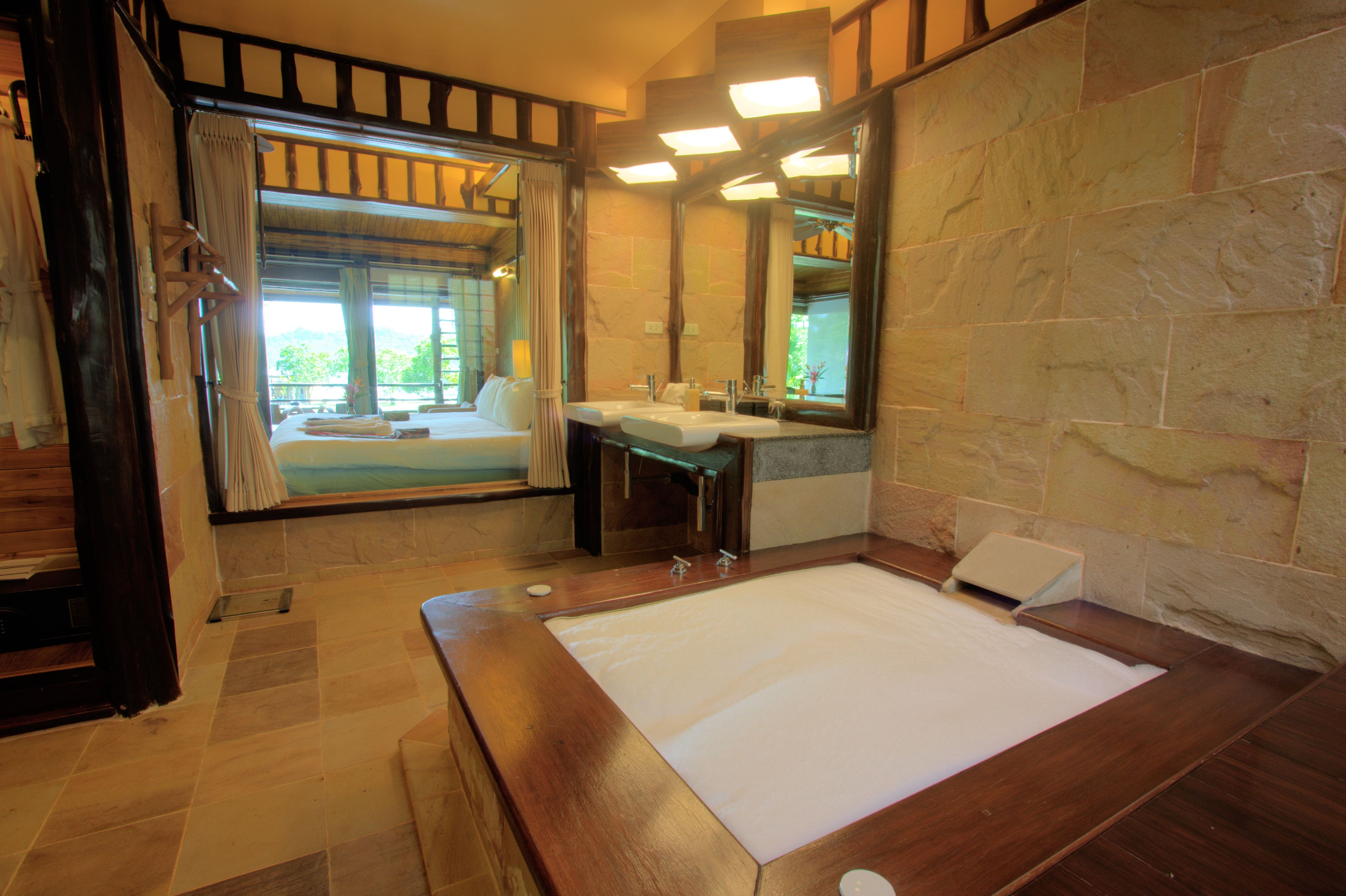 A bathroom with a large bathtub, a wooden vanity, a mirror, and a window with curtains.