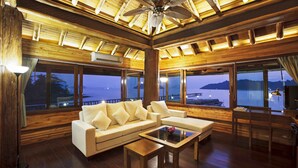 Een ruime woonkamer met een houten plafond, grote ramen en uitzicht op het water.