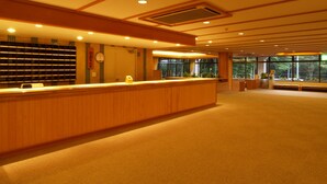 A reception area with a wooden reception desk, a clock, and a window with a view of trees. - KUROHIME KOGEN HOTEL (Shinano)