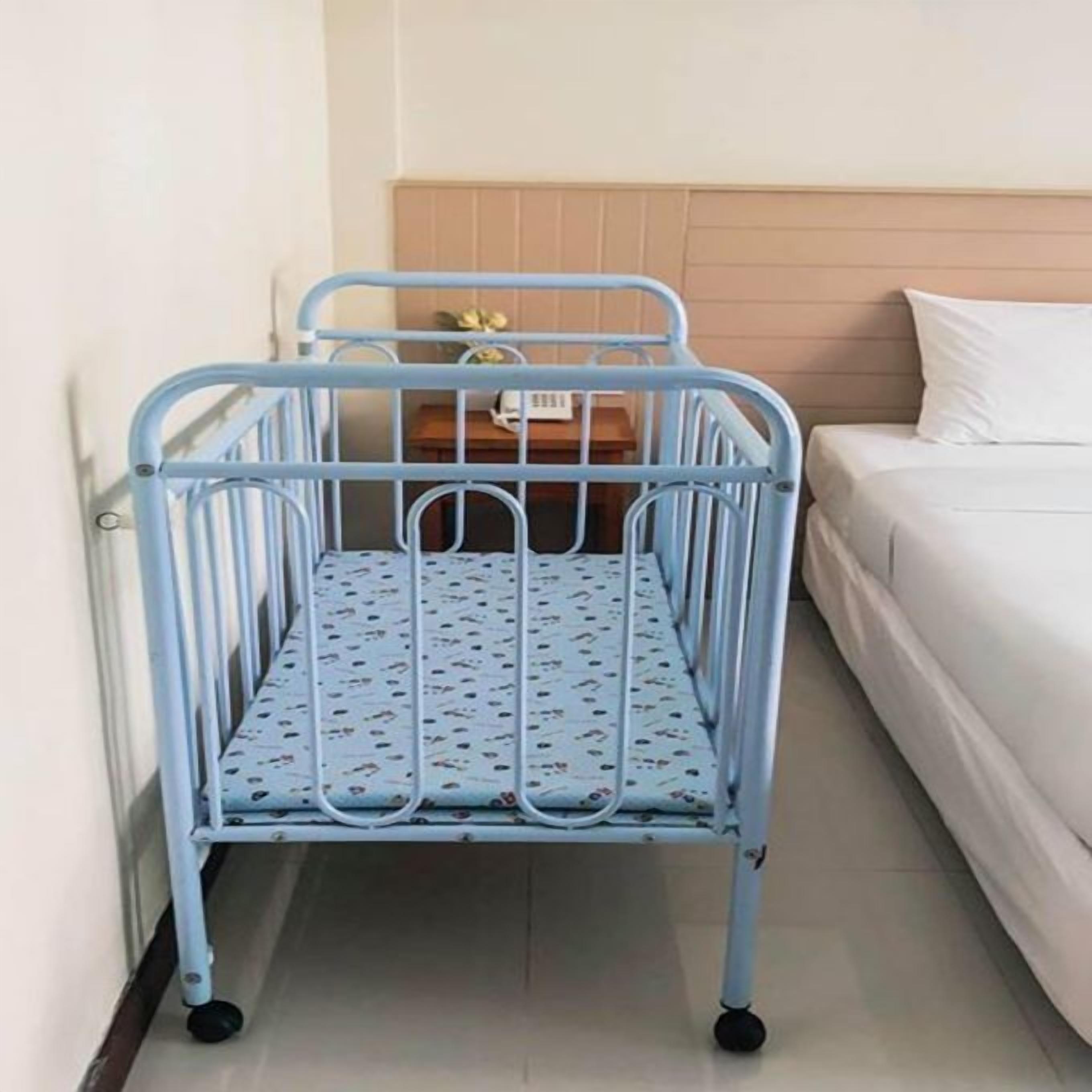 Un berceau en métal avec un matelas à motifs dans une chambre d’hôtel.