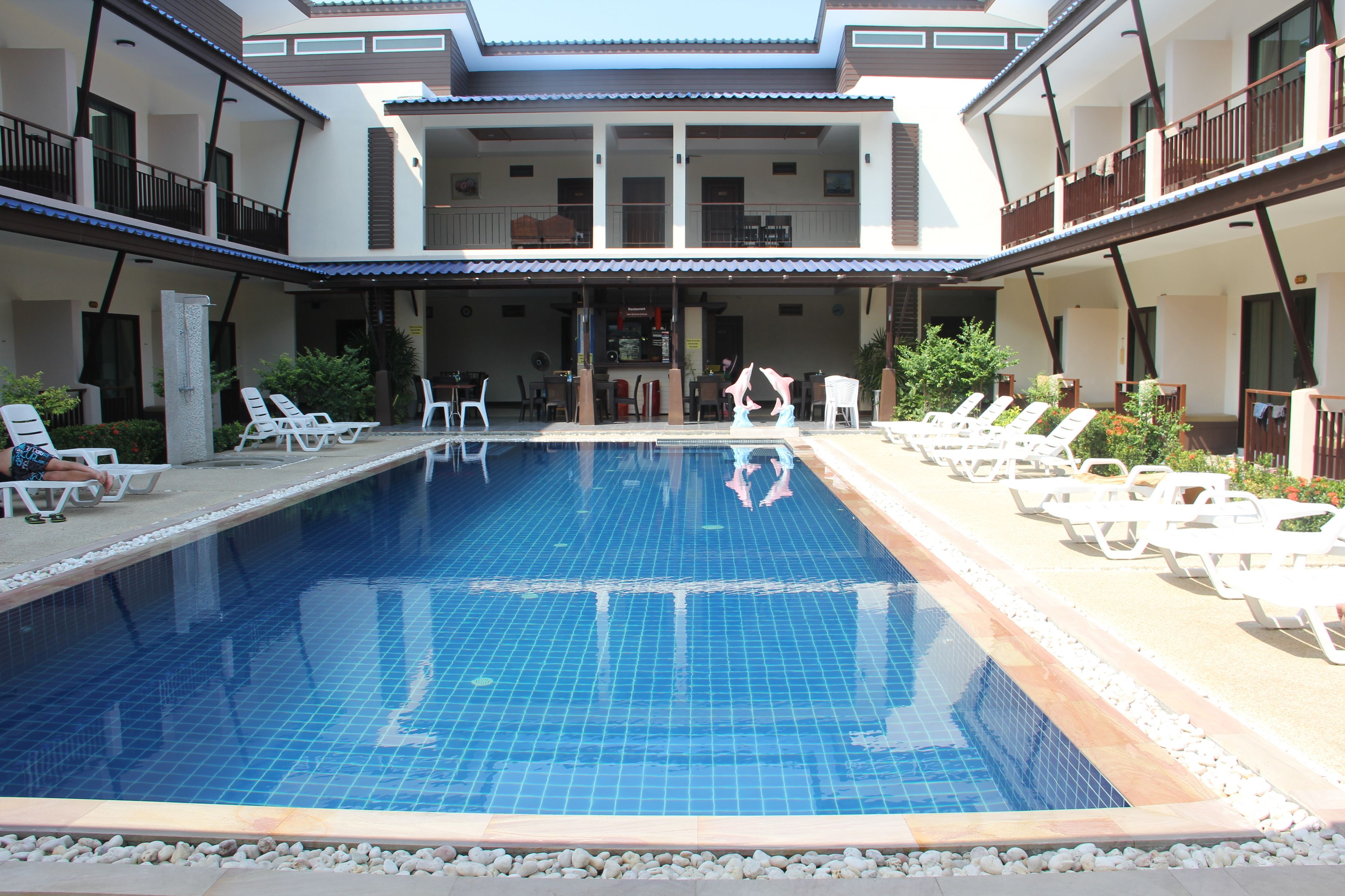 A swimming pool with lounge chairs and tables, surrounded by a building with balconies.