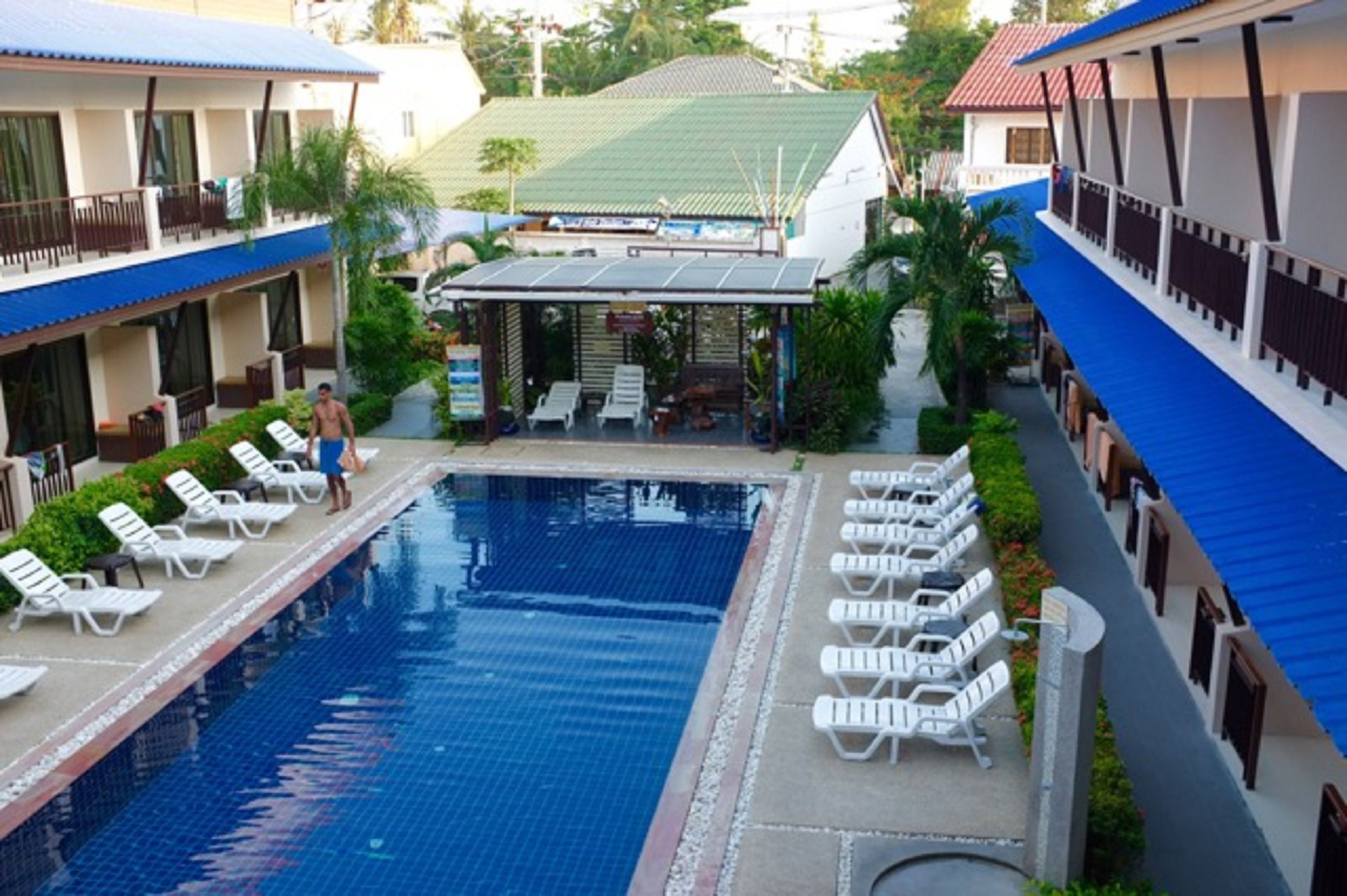 A swimming pool with lounge chairs and a covered seating area, surrounded by hotel buildings with balconies.