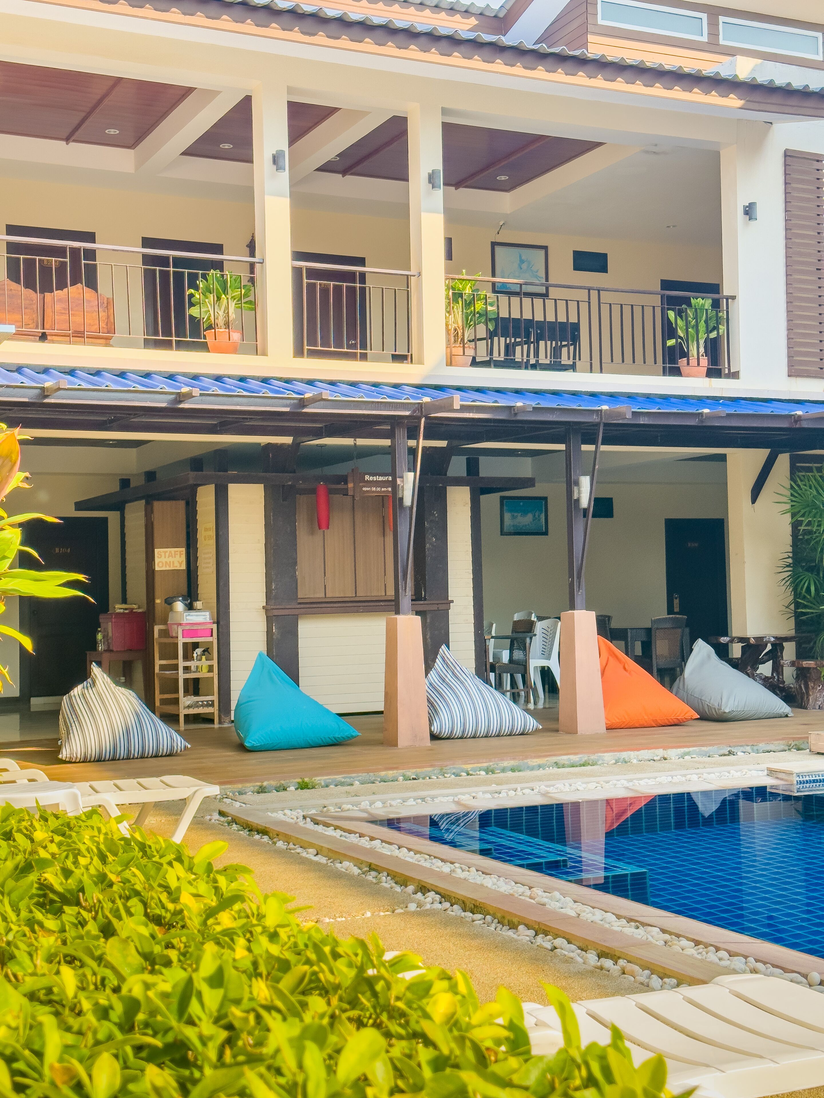 Un hotel con zona de piscina, mobiliario exterior y un porche cubierto.