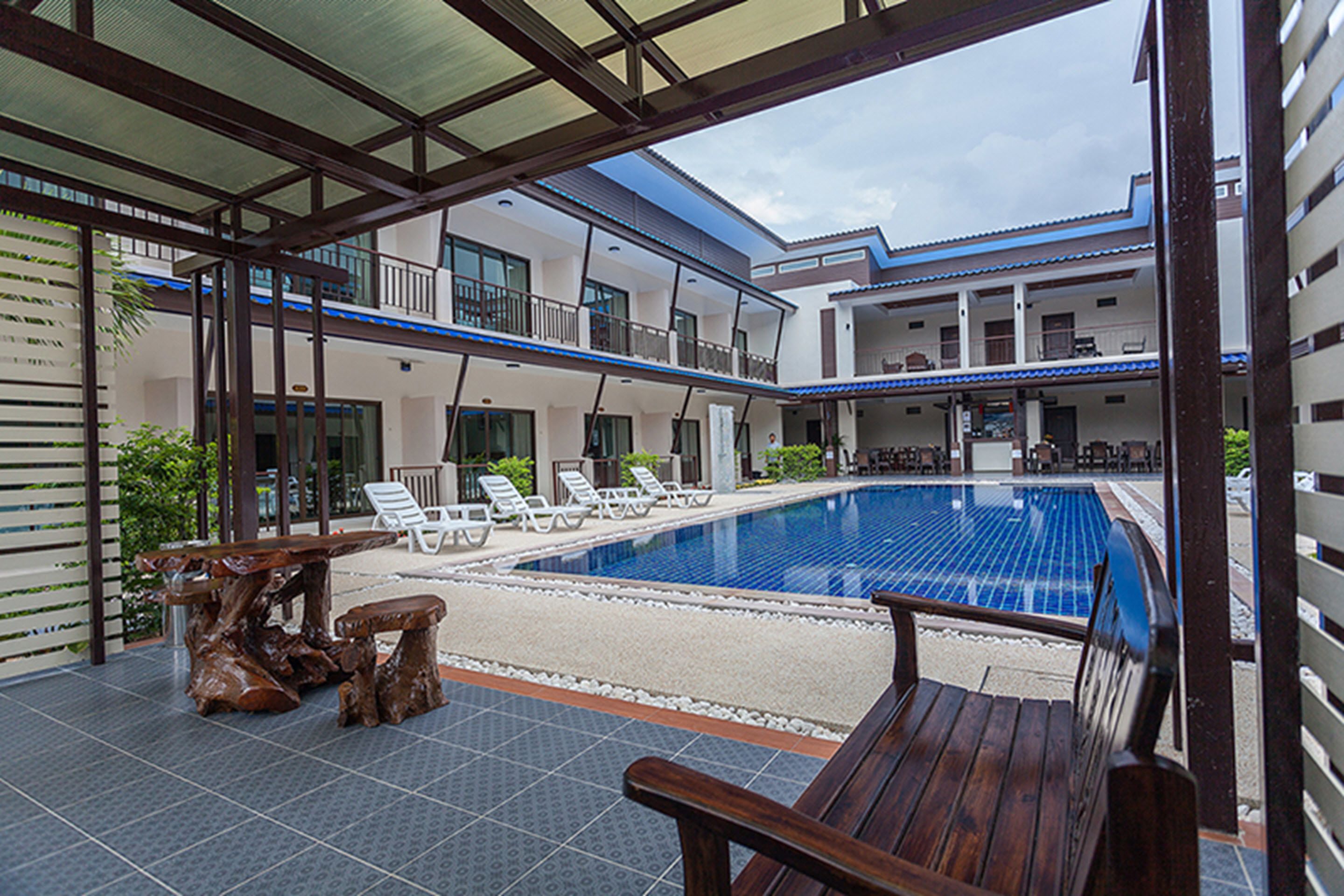 A pool area with lounge chairs, a wooden bench, and a dining table.
