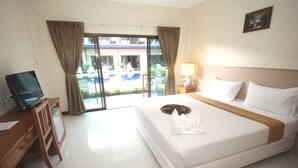 Habitación de hotel con cama, escritorio con computadora, lámpara y vista a una piscina y un edificio a través de la ventana.