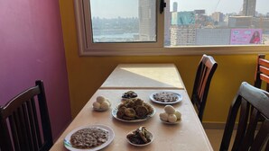 A dining table with various dishes, a window with a city view, and a pink wall. - Isis Hostel 2 (Cairo)