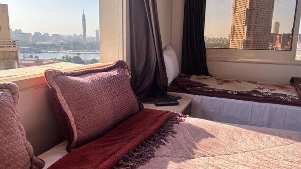 A hotel room with a bed, a window with curtains, and a view of a cityscape including a tall tower. - Isis Hostel 2 (Cairo)