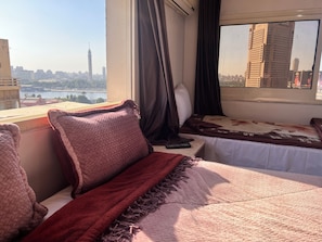 Habitación de hotel con cama, ventana con cortinas y vista a un paisaje urbano que incluye una torre alta.
