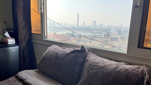 A room with a bed, a window with a view of a cityscape, a desk with a bottle and tissues, and a curtain. - Isis Hostel 2 (Cairo)