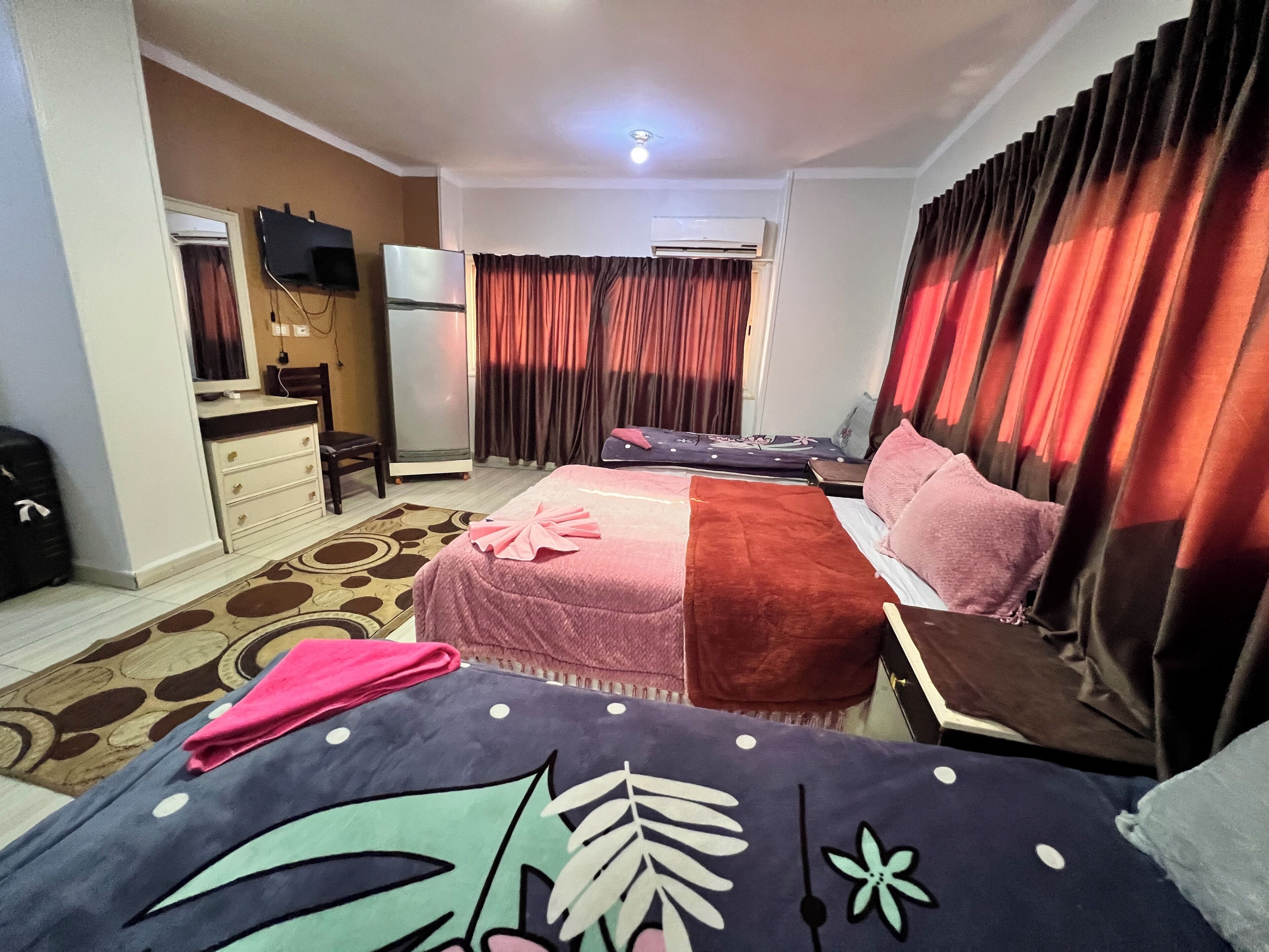 A hotel room with a bed, a desk, a chair, a television, and an air conditioning unit.