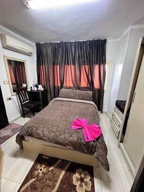 A bedroom with a bed, a desk, a chair, a wardrobe, and a window with curtains.