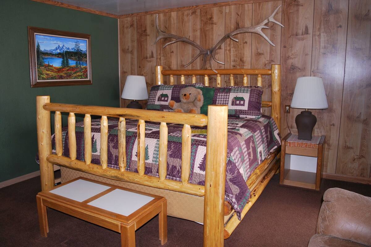 A wooden bed with a quilt, two bedside lamps, a small table, and a framed picture on the wall.