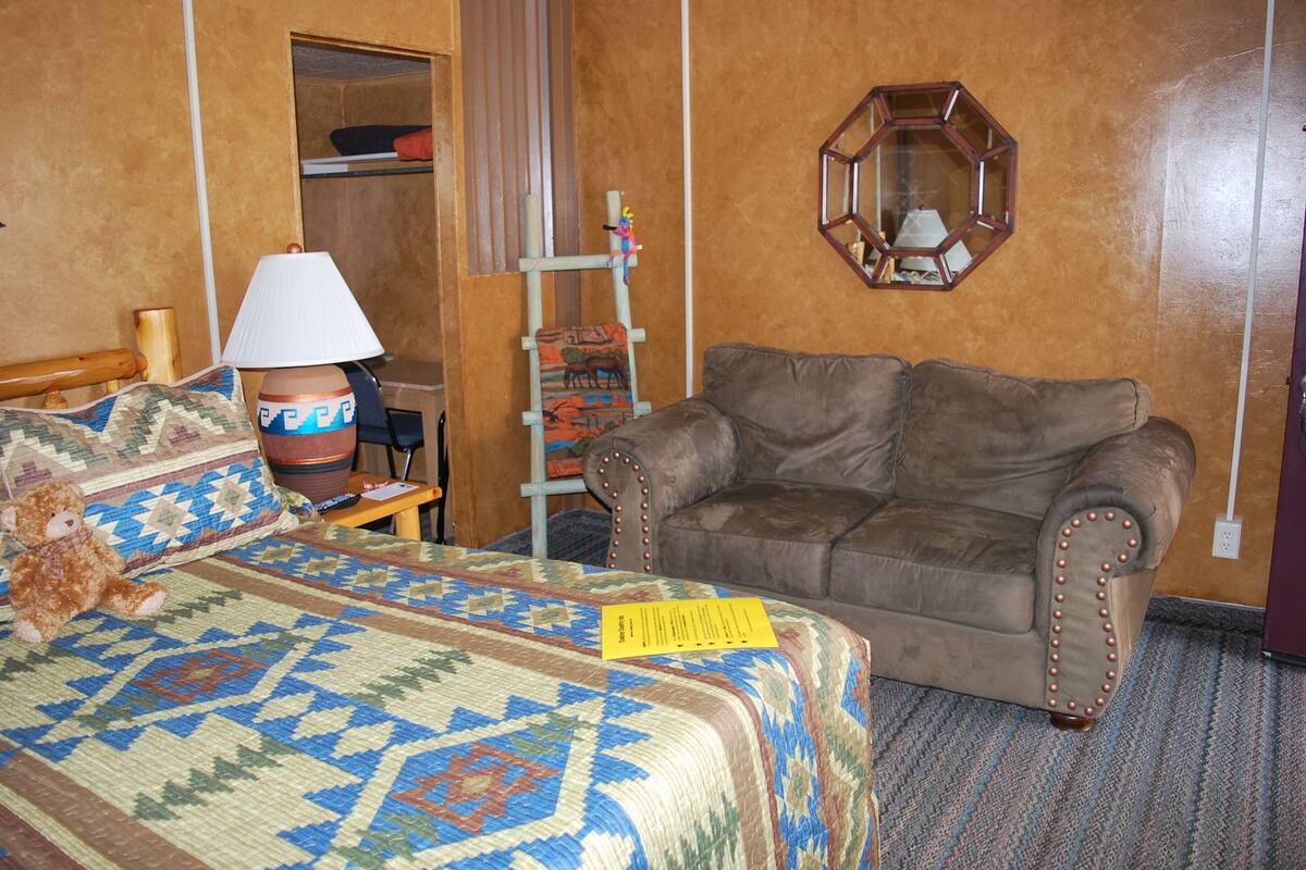 A hotel room with a bed, a brown leather sofa, a wooden ladder, a mirror, and a lamp.