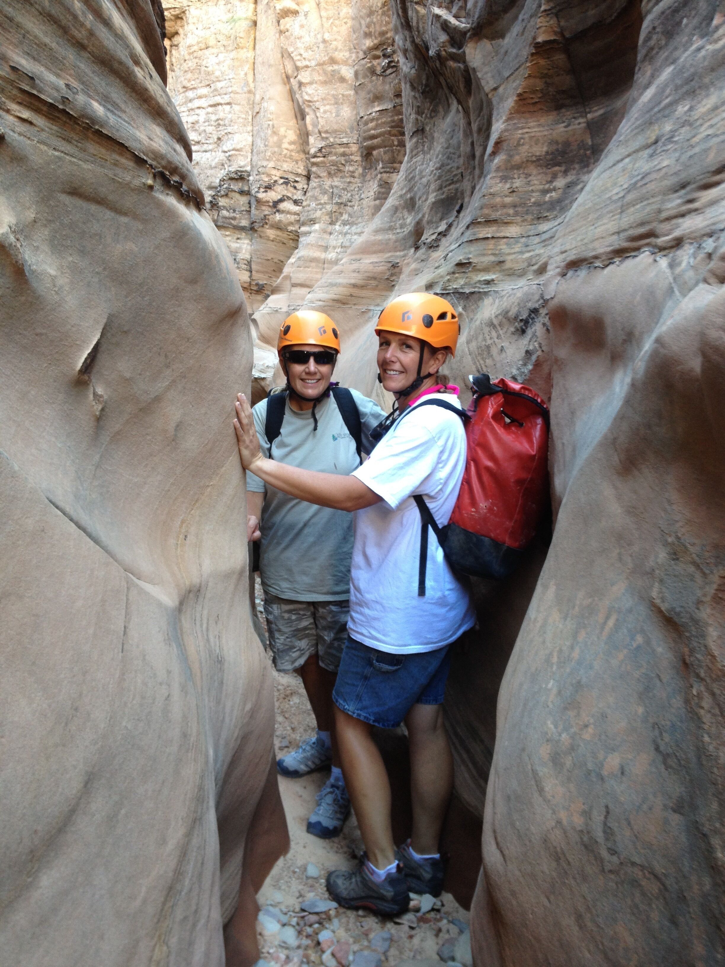 Two people in a narrow canyon with rocky walls, wearing helmets and backpacks.