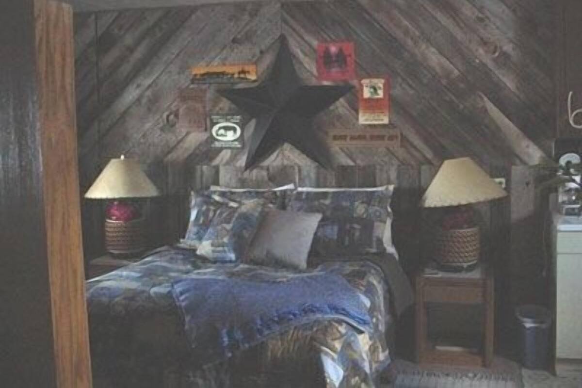A rustic bedroom with a sloped ceiling, a bed with a patterned bedspread, two bedside lamps, and a star decoration on the wall.