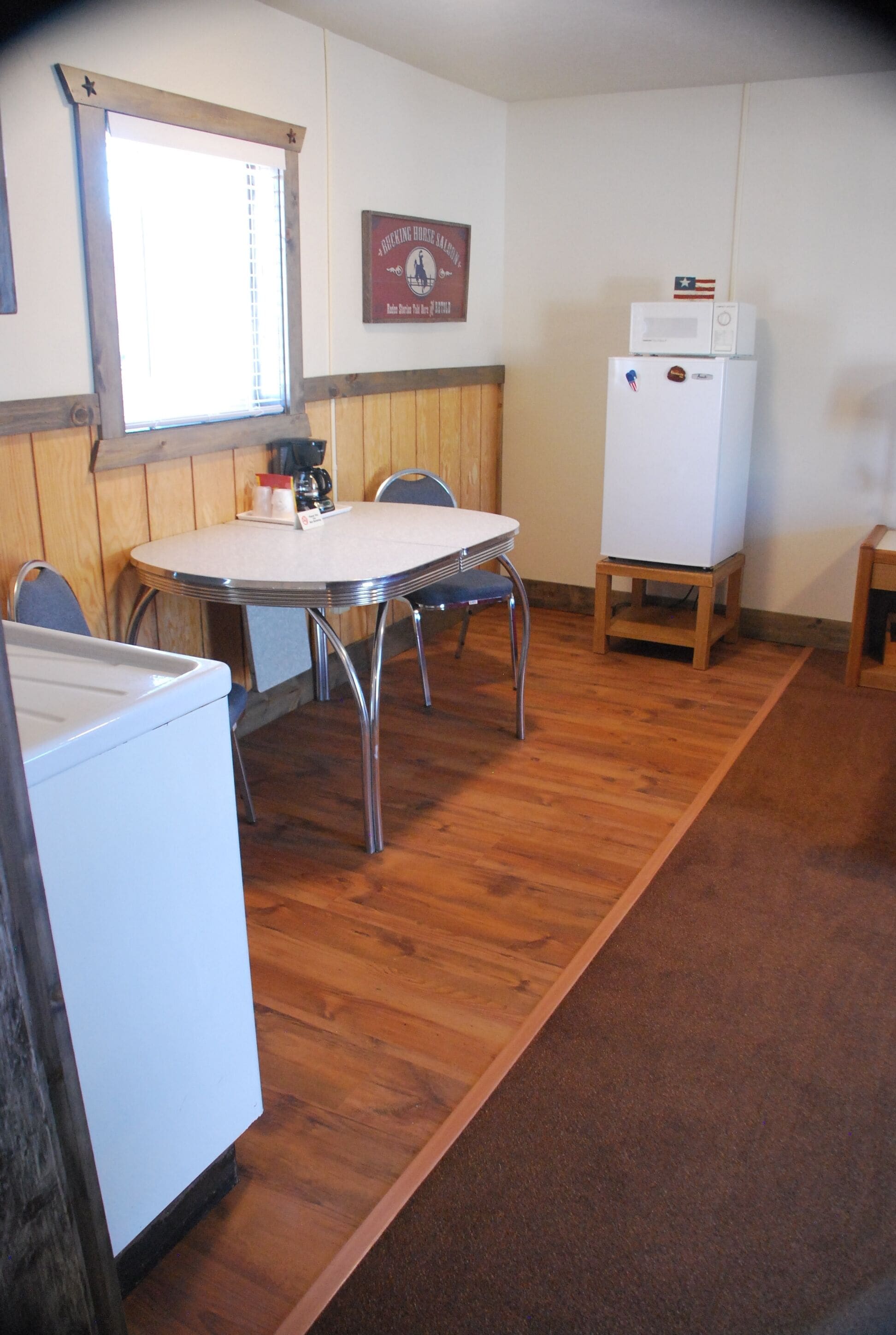 A compact kitchen with a dining table, chairs, a refrigerator, and a microwave.