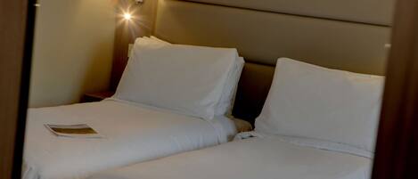 A hotel room with two single beds, a nightstand, and a lamp.