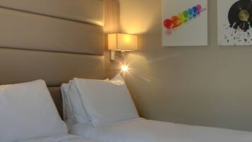 A hotel room with a bed, white linens, a wall-mounted lamp, and a framed picture of a vinyl record.