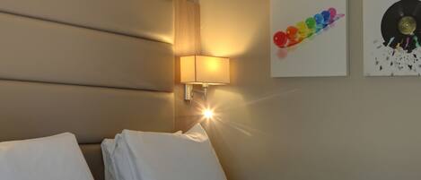 Habitación de hotel con cama, ropa de cama blanca, lámpara de pared e imagen enmarcada de un disco de vinilo.