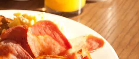 Un plato de desayuno con tocino, frijoles y tostadas, un vaso de jugo de naranja y una taza de café sobre una mesa de madera.