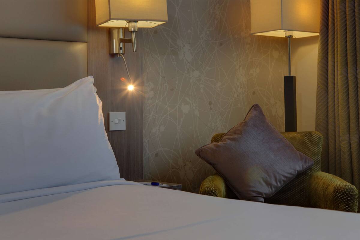 A hotel room with a bed, a nightstand, a lamp, and a chair.