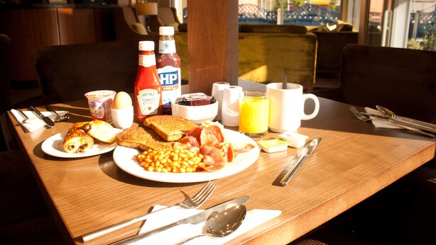A breakfast table with plates of toast, eggs, beans, and bacon, along with condiments and a coffee cup. - Best Western Pontypool Metro Hotel (Pontypool)