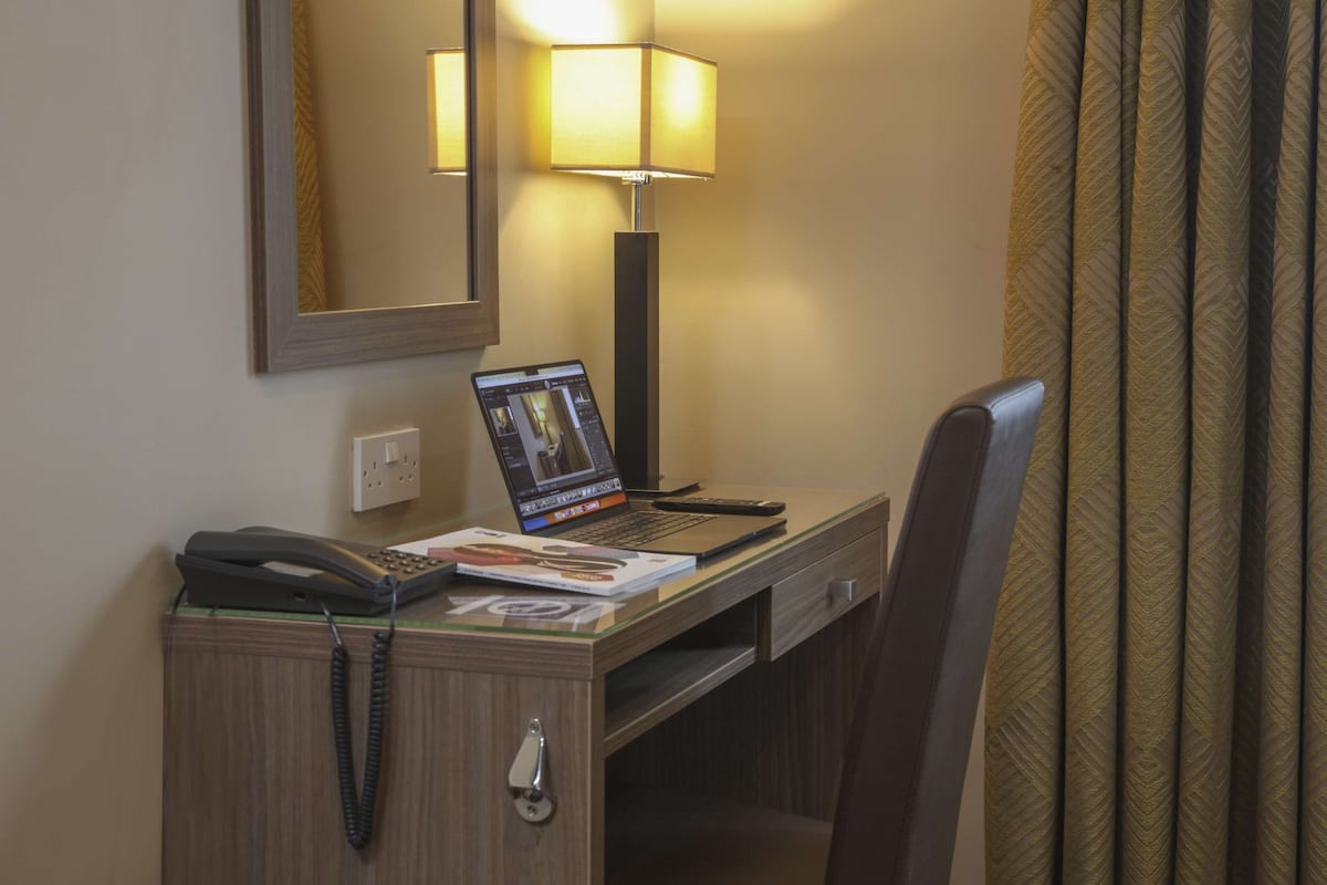 A hotel room desk with a laptop, a phone, and a magazine.
