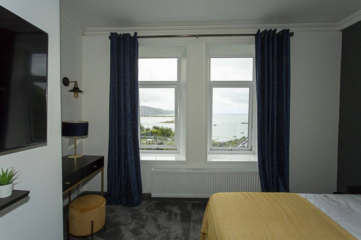 Ein Zimmer mit Bett, Schreibtisch, Lampe und Meerblick.