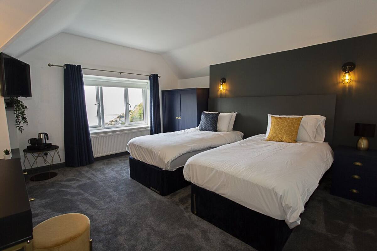 Ein Hotelzimmer mit zwei Betten, einem Fernseher, einem kleinen Tisch und einem Fenster mit Vorhängen.