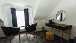 Una habitación pequeña y moderna con un escritorio, dos sillas, un espejo redondo, un taburete pequeño y una ventana con cortinas.