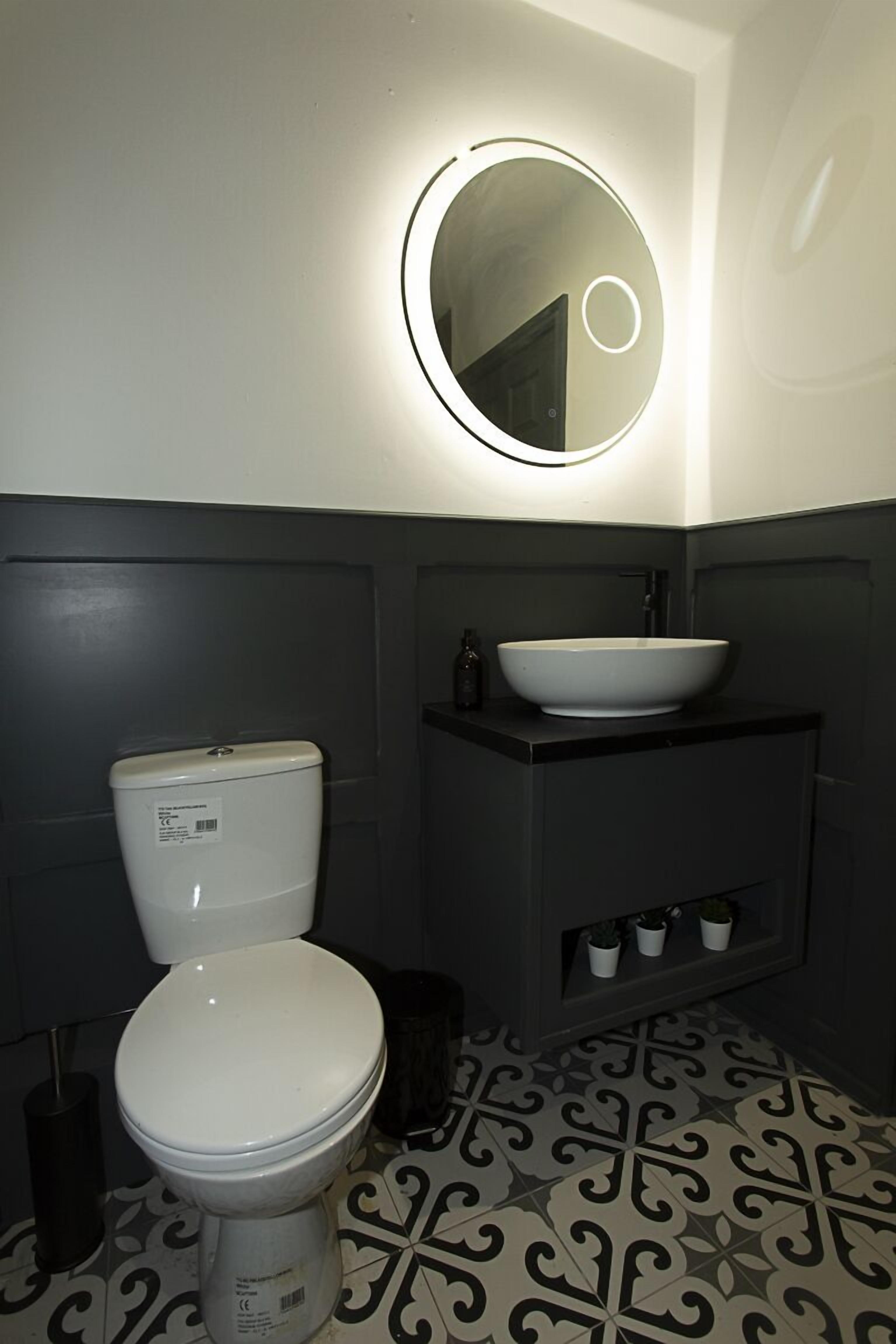 Een badkamer met toilet, wastafel, spiegel en een vloer met patroon.
