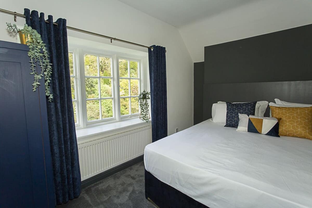 Ein Schlafzimmer mit einem großen Bett, einem Fenster mit Vorhängen, einem Heizkörper und einem dunklen Kopfteil.