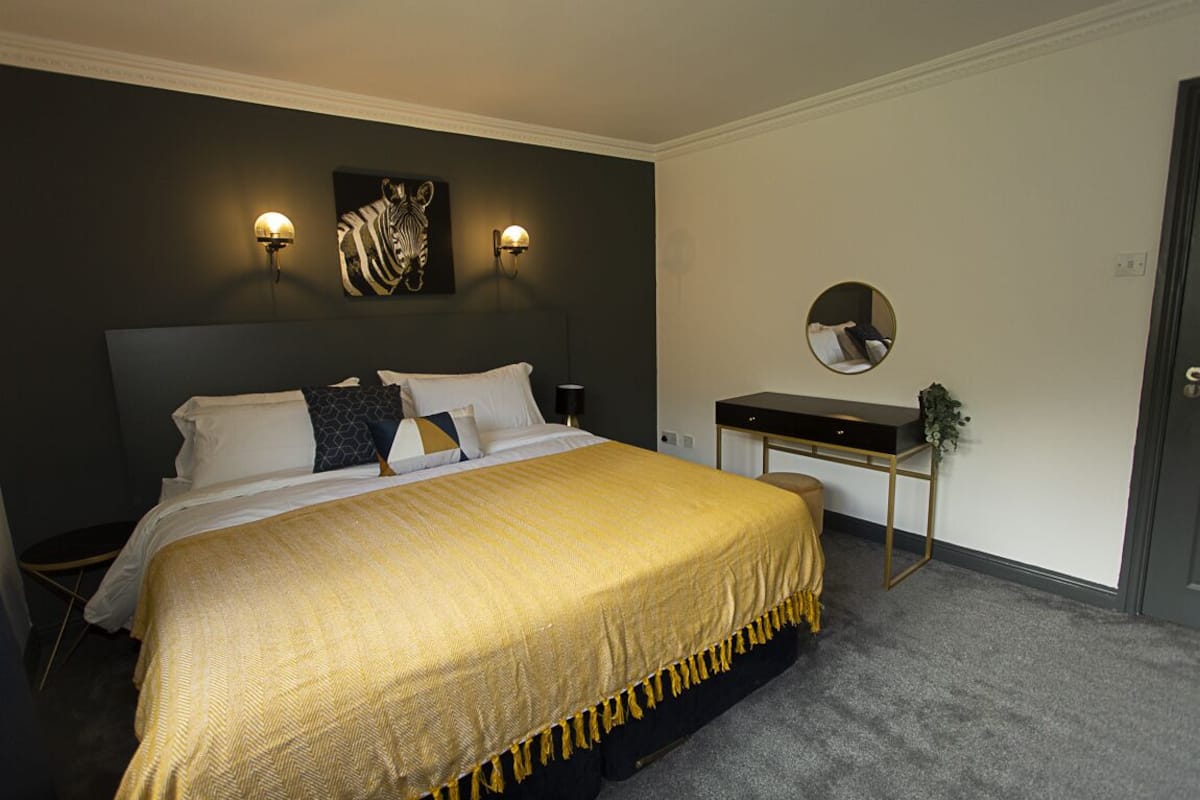 Ein Schlafzimmer mit einem großen Bett, zwei Wandleuchten, einem runden Spiegel und einem kleinen Schreibtisch mit einer Pflanze.
