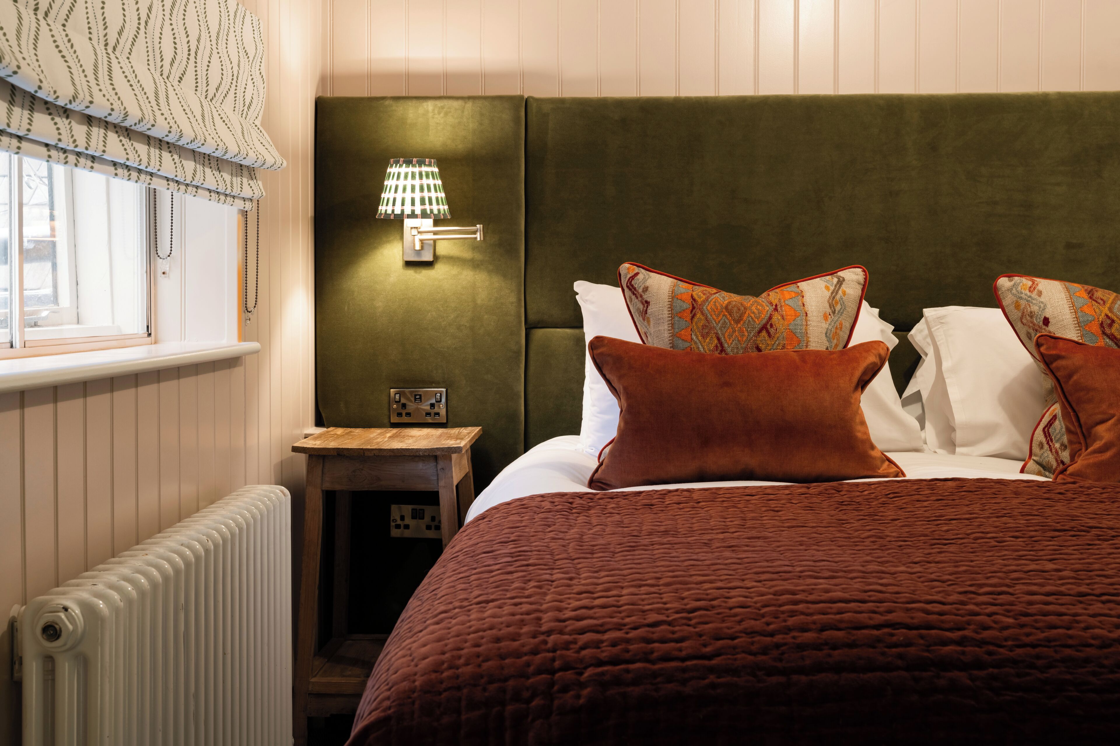 A bedroom with a green headboard, a bedside table with a lamp, and patterned pillows.
