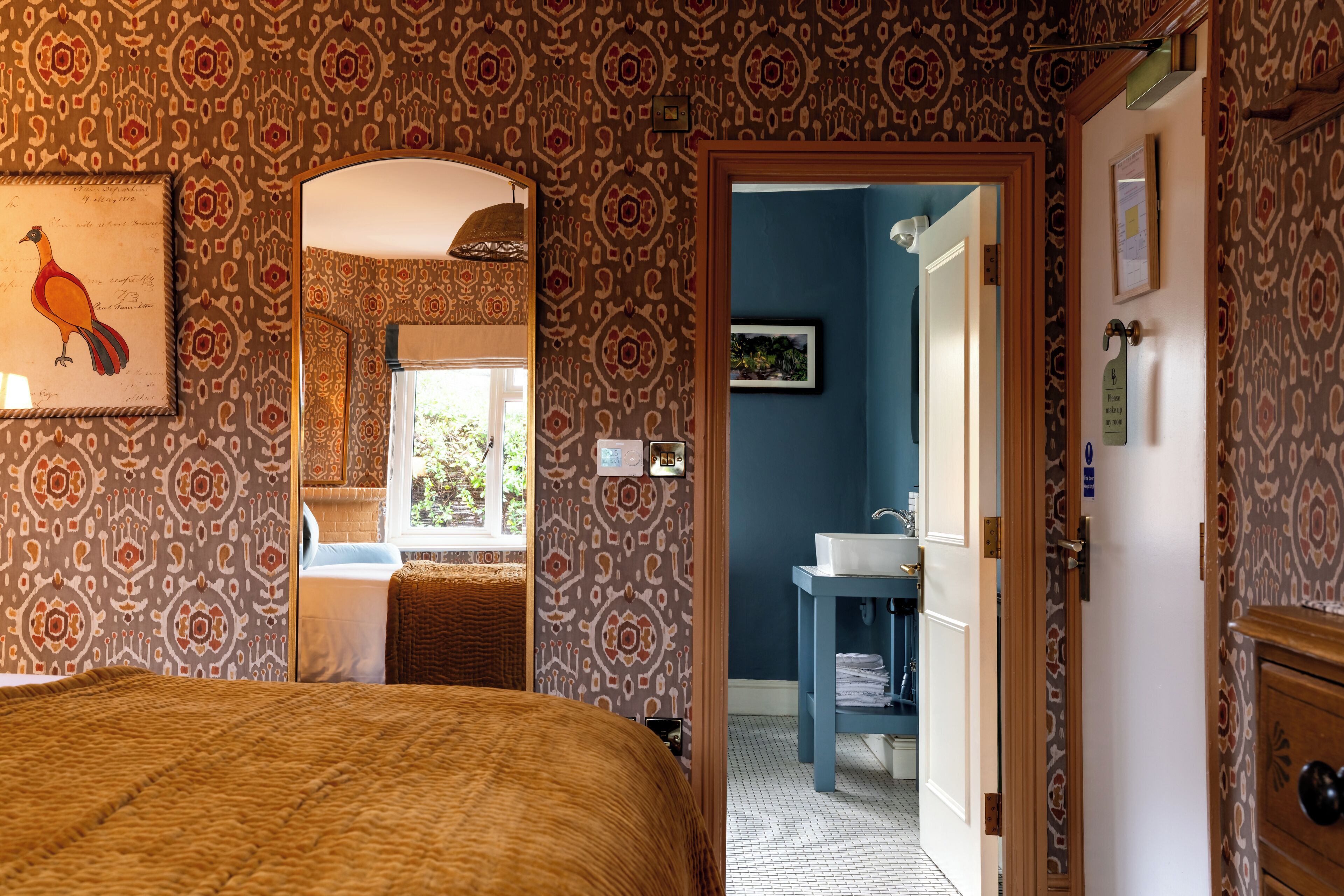 Un dormitorio con papel tapiz estampado, una cama, un espejo y vistas al baño.