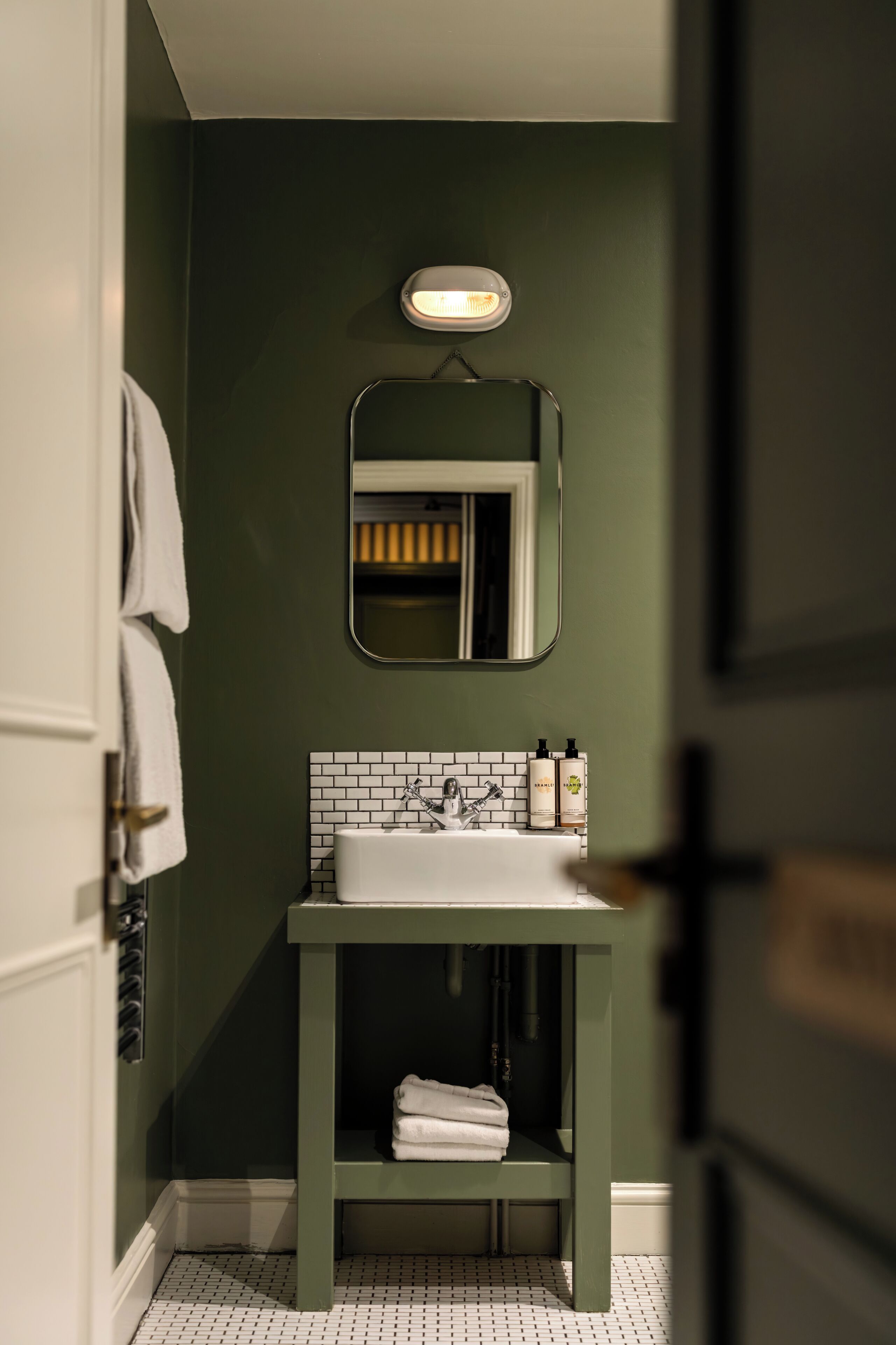Un baño con lavamanos blanco, paredes verdes, un espejo y un perchero para toallas.
