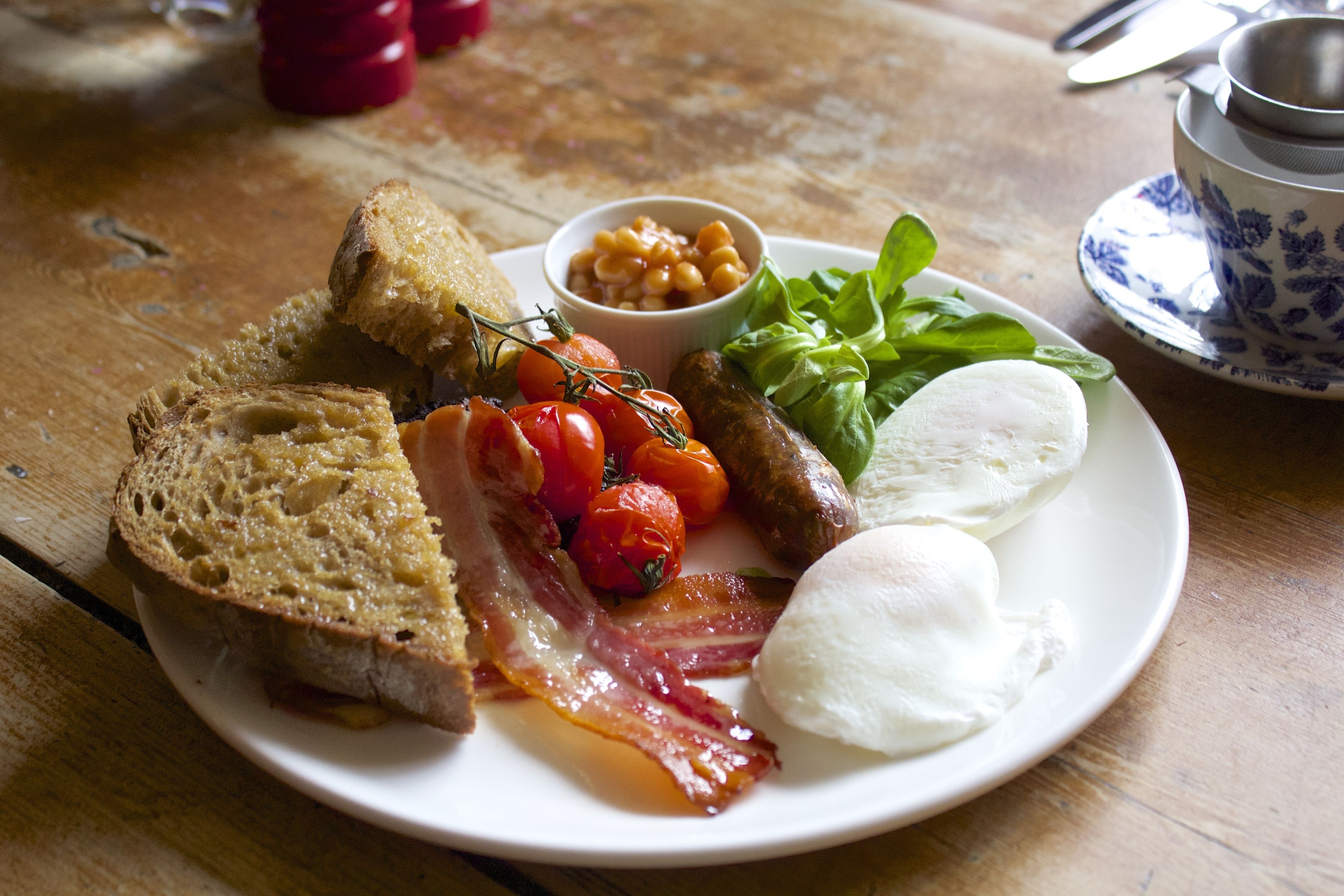 A plate of breakfast with toast, bacon, eggs, tomatoes, beans, and greens.