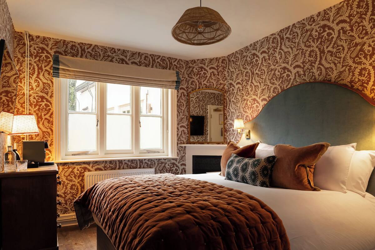 A bedroom with a large bed, a dresser, a window with curtains, a mirror, and a hanging light fixture.