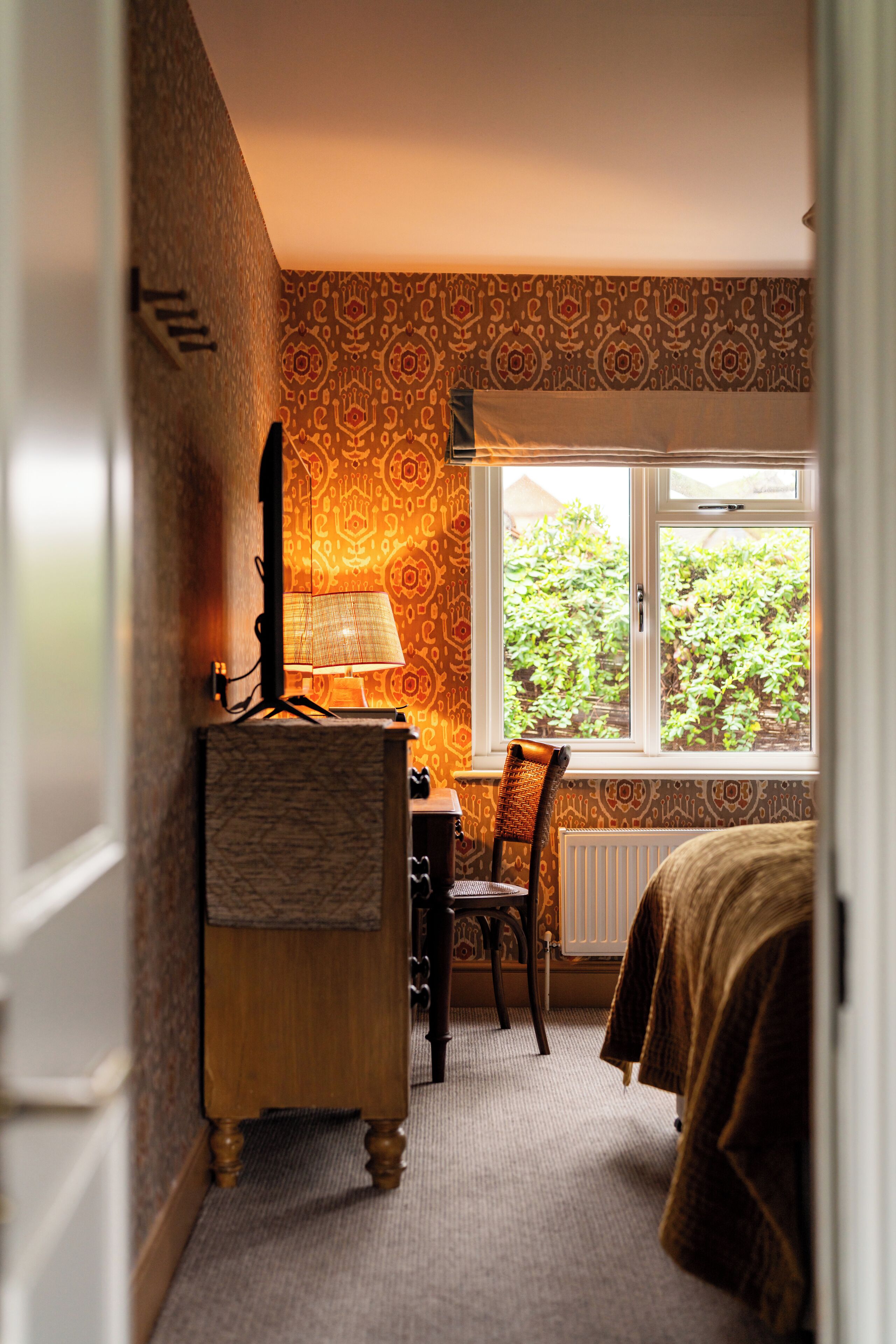 A bedroom with a dresser, a chair, a lamp, and a window with a view of greenery.