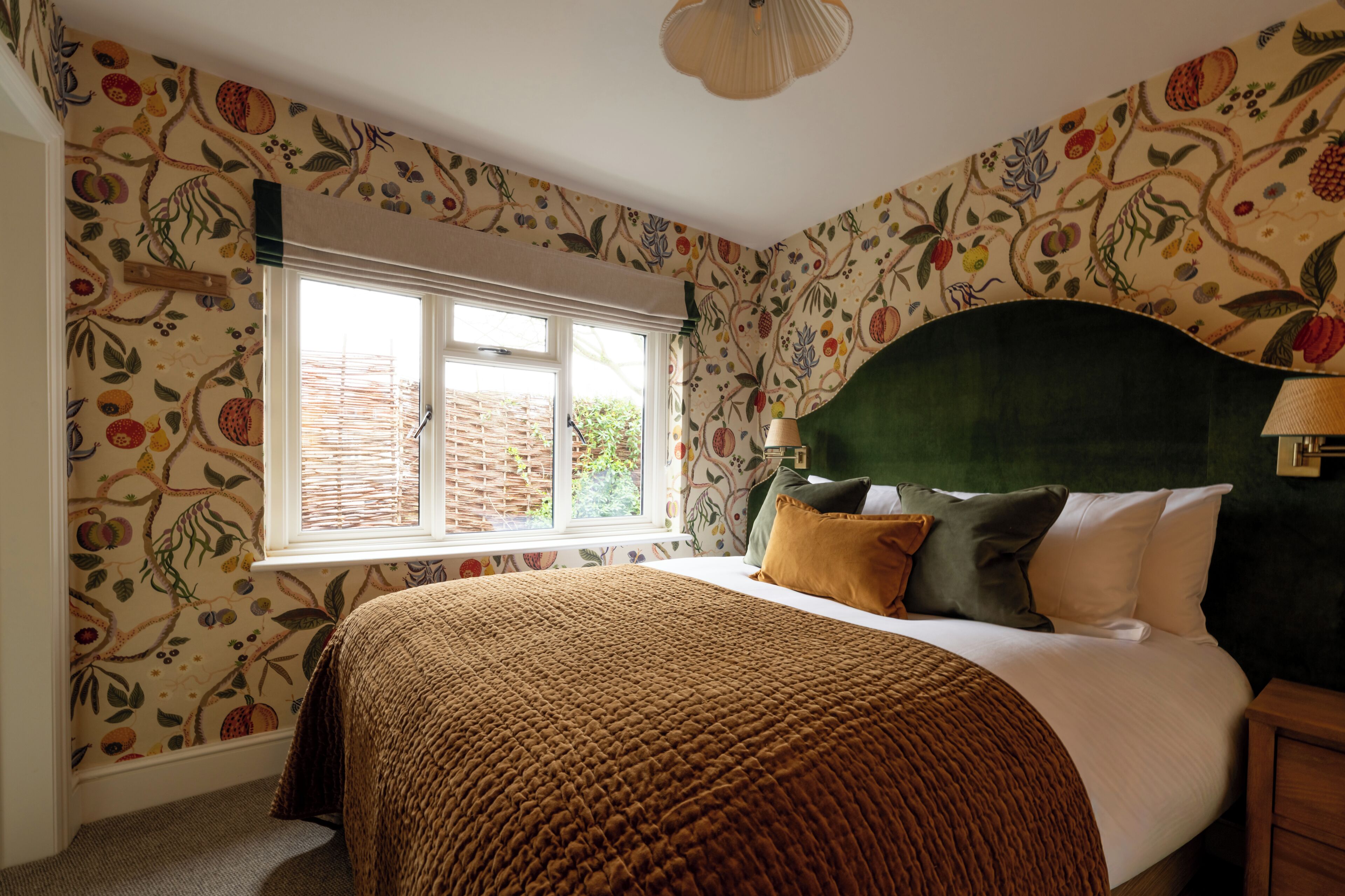 Een slaapkamer met een groot raam, een bed met een groen hoofdeinde en behang met een patroon.