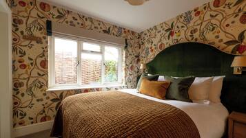 Een slaapkamer met een groot raam, een bed met een groen hoofdeinde en behang met een patroon.