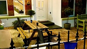 A brick building with a white door, a staircase, and a small garden area with a table and chairs. - Devon House Guest House (Paignton)