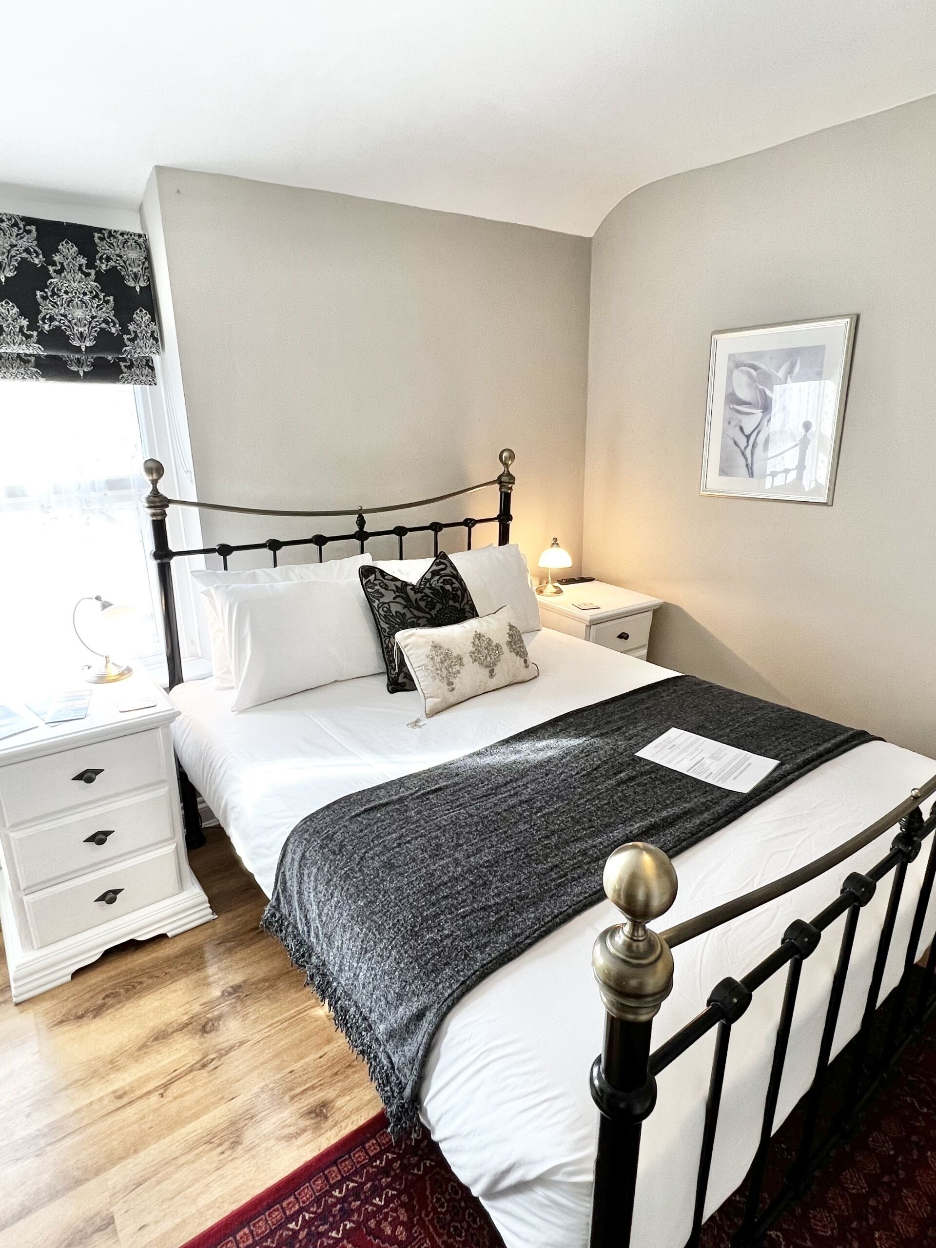 A neatly arranged bedroom with a bed, bedside tables, a nightstand, a lamp, and a framed picture on the wall.