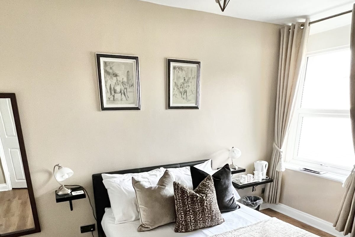 Un dormitorio ordenado con cama, mesitas de noche, lámpara de techo con forma de estrella y dos cuadros en la pared.