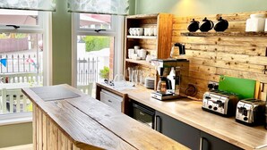 A kitchen with wooden cabinetry, a wooden bar counter, and a view of the outside. - Devon House Guest House (Paignton)