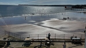 A beach view with a pier, people walking, and a grassy area with a fence. - Devon House Guest House (Paignton)