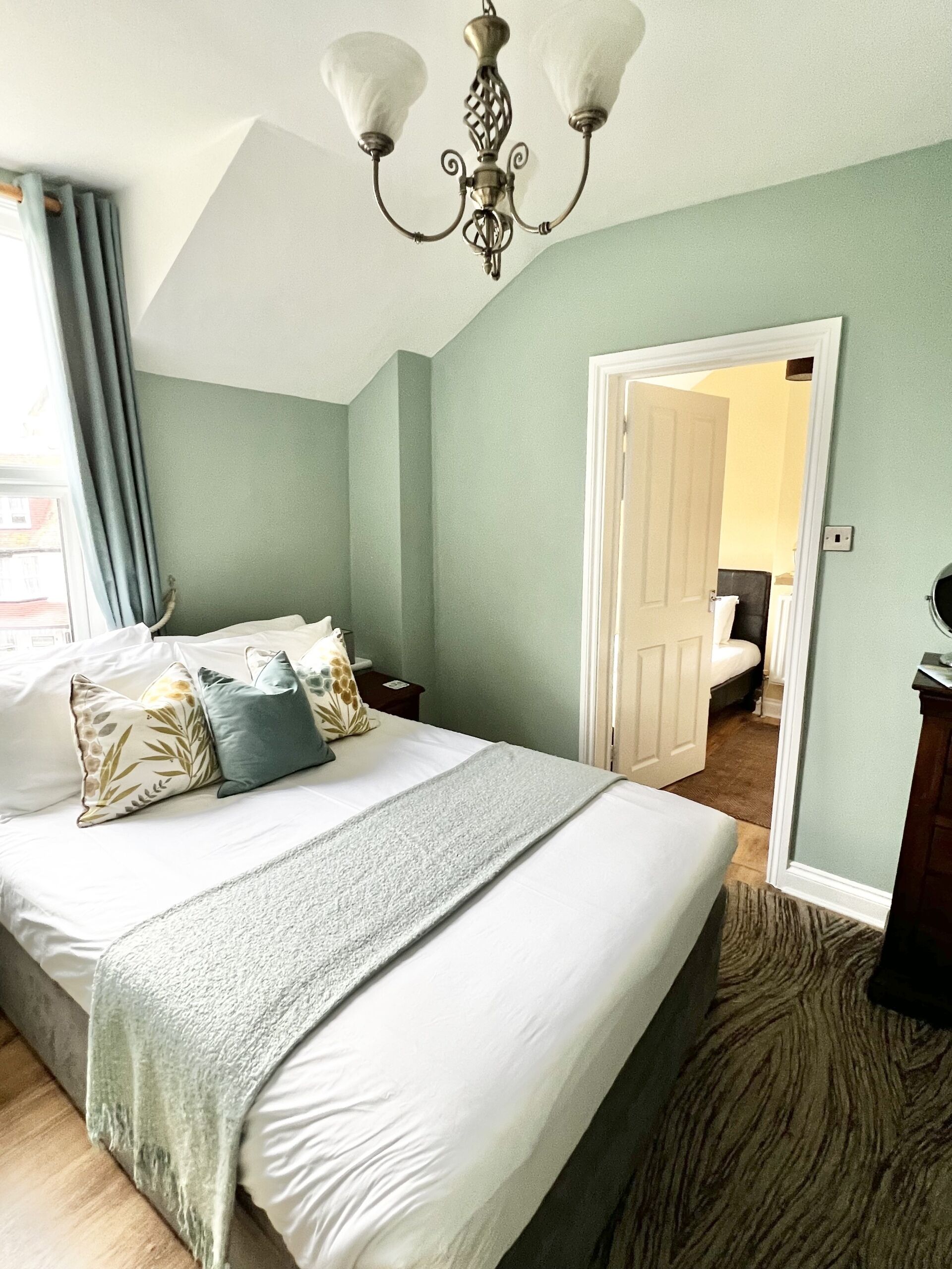 Un dormitorio con cama, un candelabro, una puerta y vista a otra habitación.