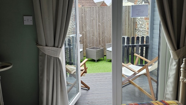 A bedroom with a bed, two rolled towels, and a colorful blanket. There is a sliding glass door leading to an outdoor area with a wooden fence and a sign. - Hooray Henrys Sheringham (Sheringham)